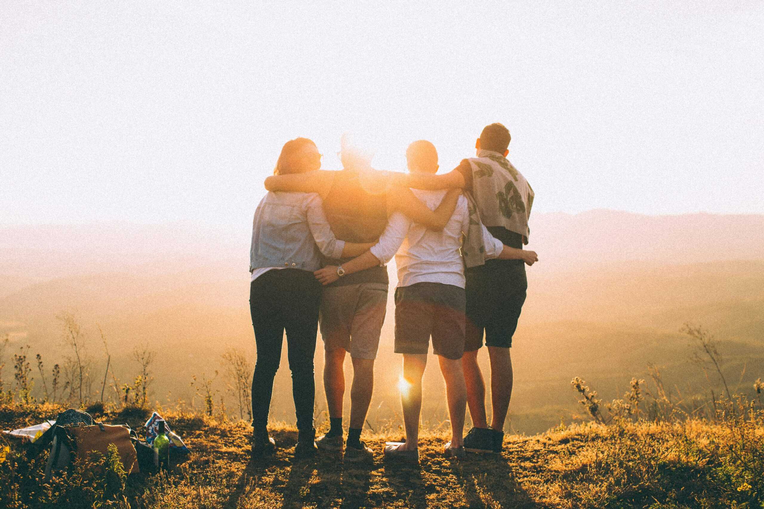 Vier Menschen die sich umarmen und in die Sonne schauen